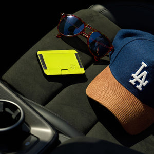 Yellow Maverick minimalist cardholder, sunglasses, and a cap with a logo on a car's black interior.