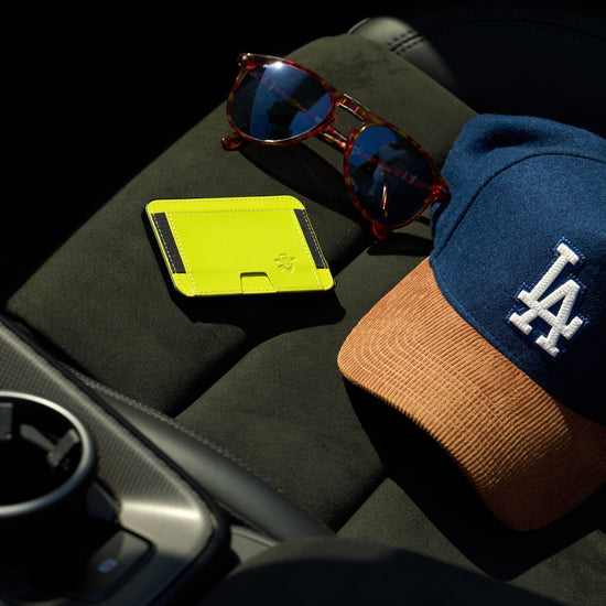 Yellow Maverick minimalist cardholder, sunglasses, and a cap with a logo on a car's black interior.